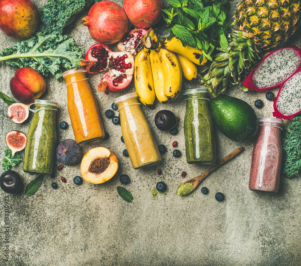 瓶子里的五颜六色的冰沙，混凝土背面有新鲜的热带水果和蔬菜