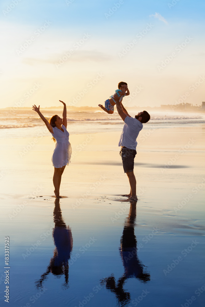 父亲在空中高高抛婴儿儿子，母亲在水池旁跳跃。快乐的一家人在阳光下漫步