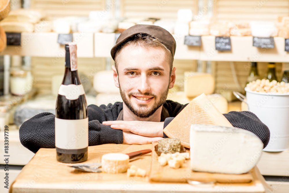 Close-up portrait of a young sommelier or cheese seller with cheese assortment and wine bottle in fr
