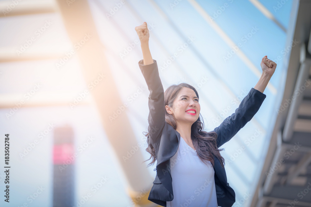 商业女性举起双臂微笑的肖像在模糊的城市背景下庆祝。商业成功