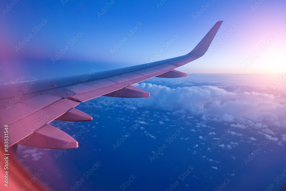 从乘客座位上看，在壮观的日落光线下，飞机在云层上方飞行。