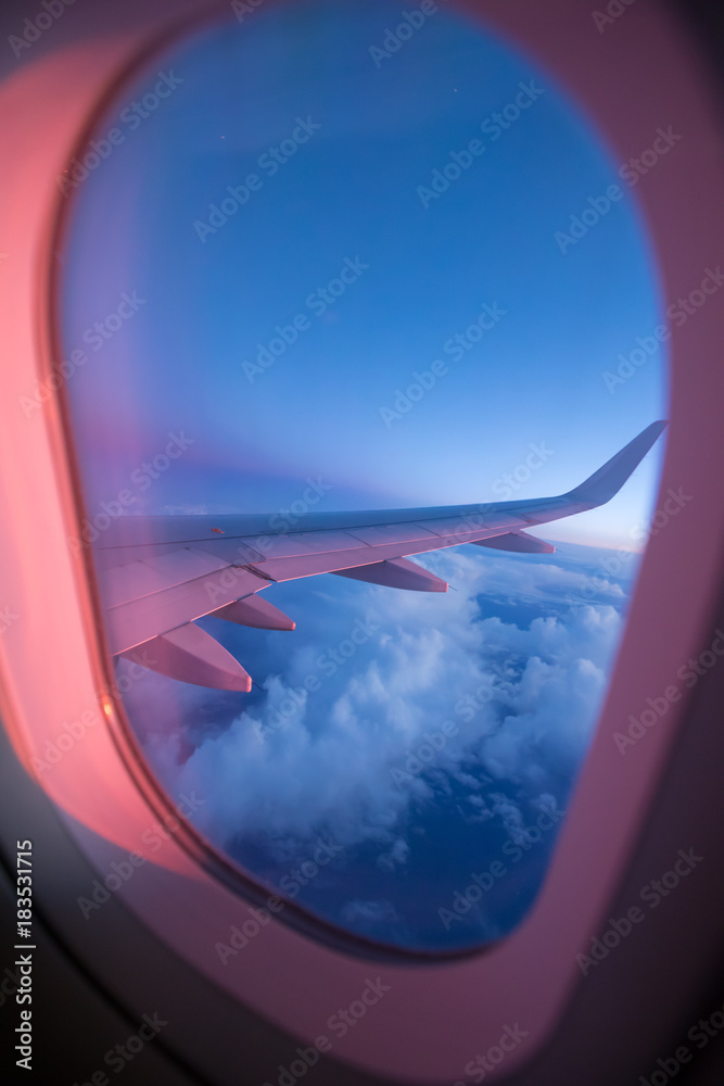 从乘客座位上观看，飞机在壮观的日落光线下在云层上方飞行。