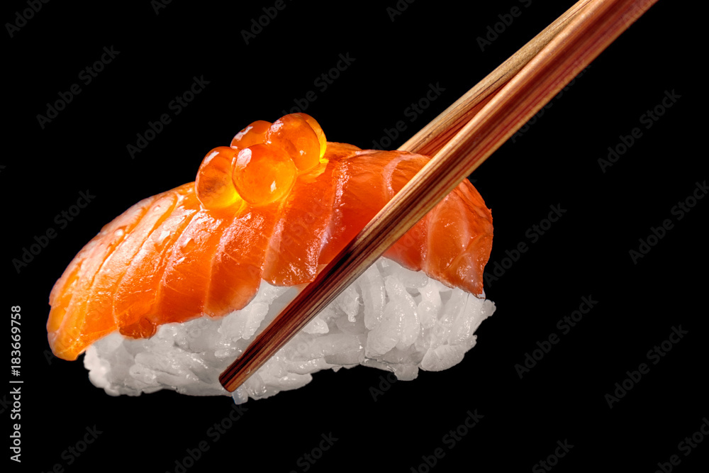 筷子里的三文鱼寿司nigiri被隔离在黑色背景上。特写。