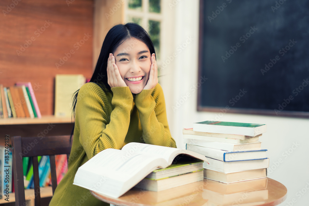 快乐的亚洲女学生在课间休息时在现代的书架旁看书