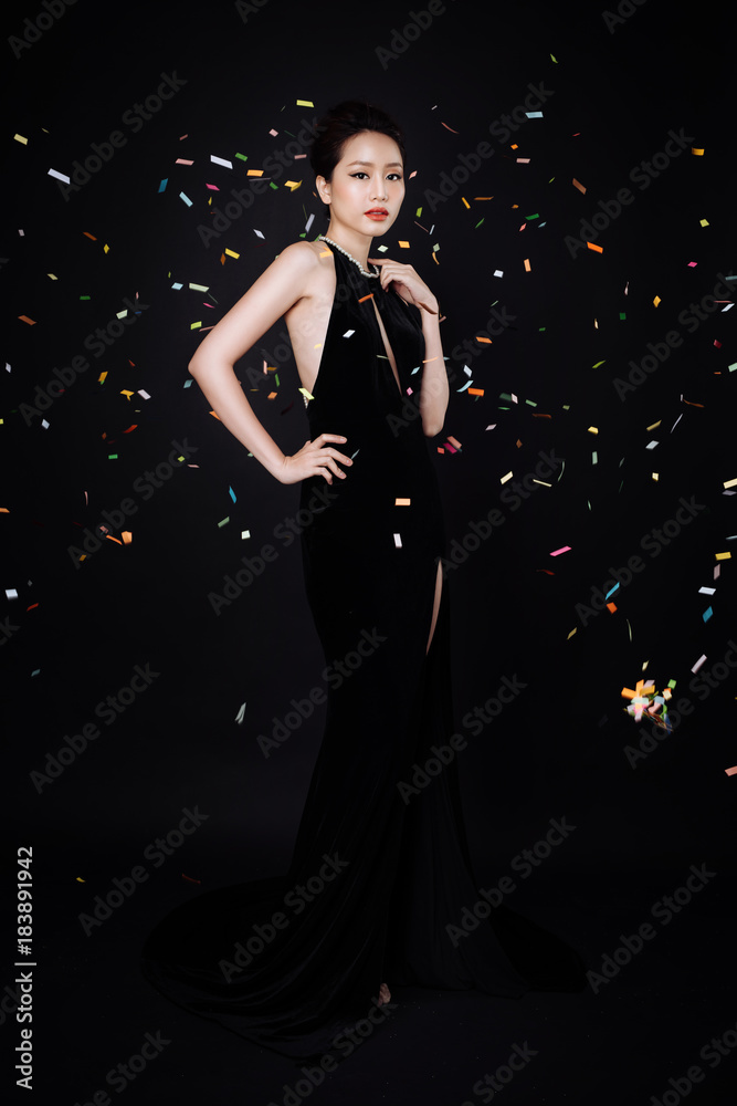 一位亚洲女性，化着时尚的妆，穿着奢华的黑色连衣裙，五彩纸屑落在她身上。