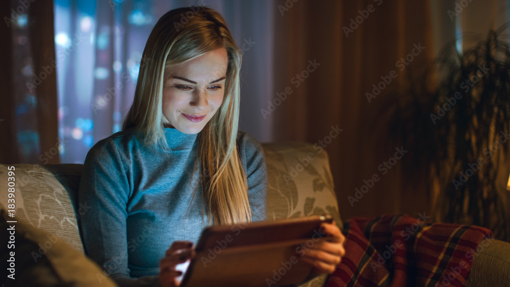 客厅里的漂亮年轻女人。她坐在沙发上，使用平板电脑。H后面