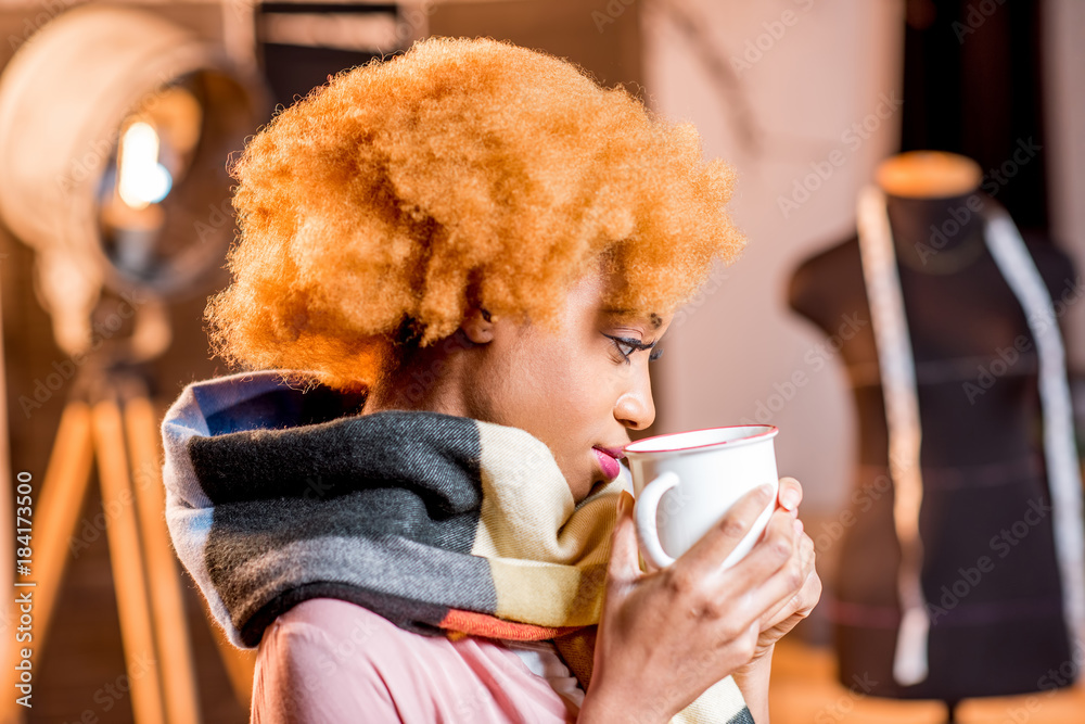 Portrait of a young african creative person with colorful scarf holding hot drink at the studio inte