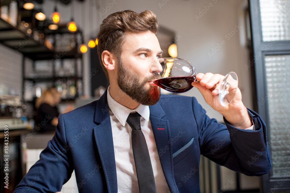 英俊的商人穿着西装坐在餐厅喝红酒