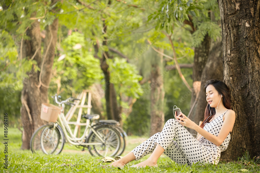 亚洲女性在公园户外的生活方式，使用智能手机听音乐放松和快乐