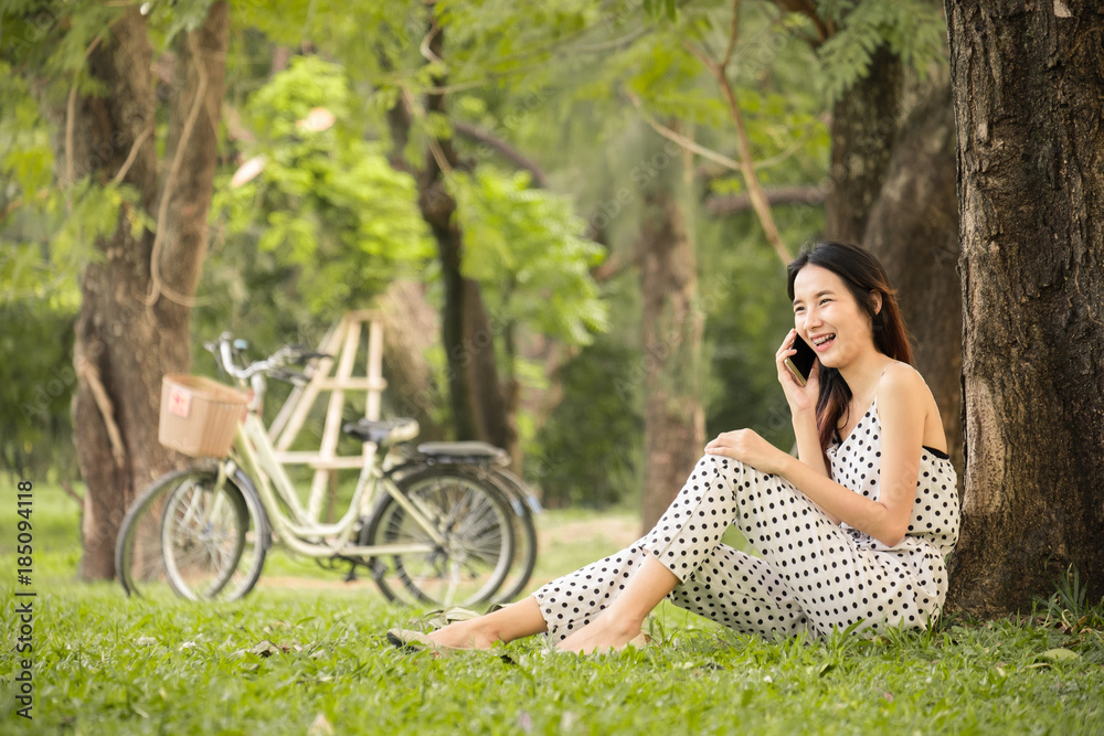 亚洲女性在公园户外的生活方式，使用智能手机和聊天来放松和快乐