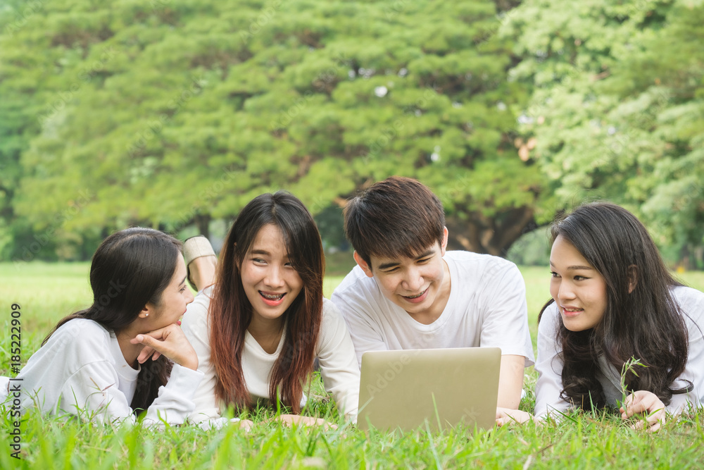 Group of Asian students laying on grass outdoor park, with laptop books and happy smile for friendsh