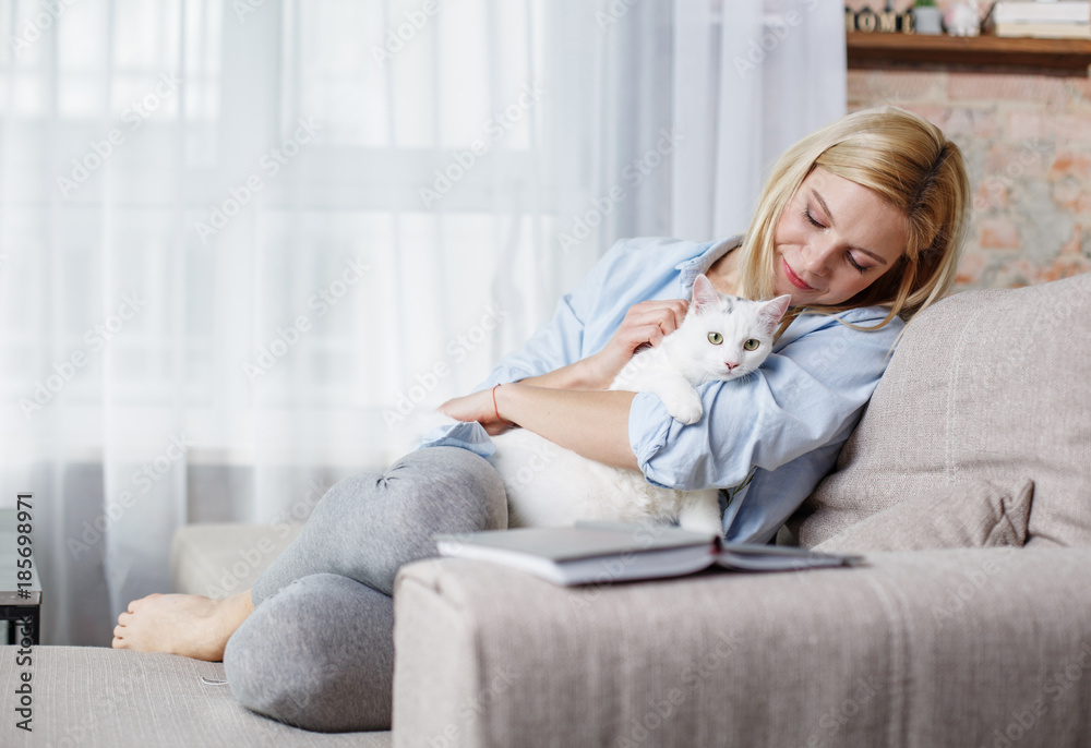 友谊概念。幸福女人在家里沙发上放松，拥抱宠物的全长肖像。
