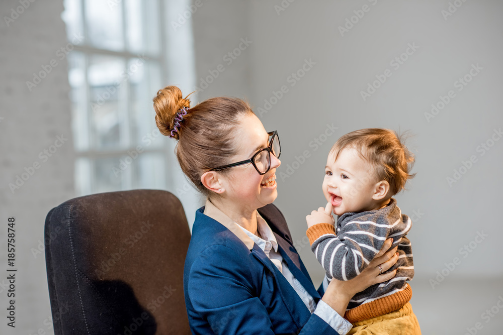 年轻的多任务女商人穿着西装在办公室和她的小儿子玩得很开心