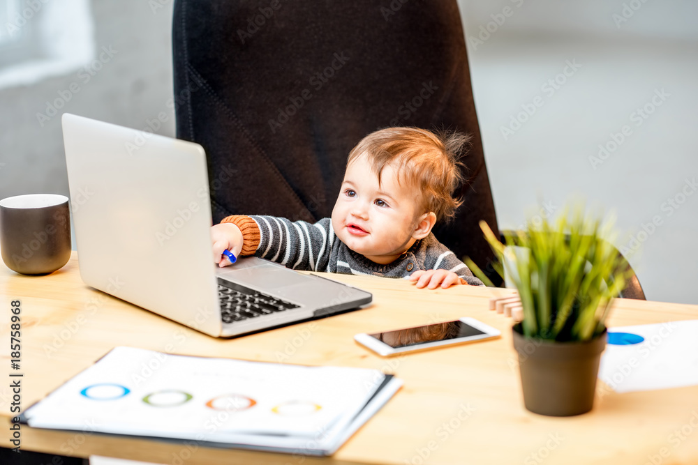 婴儿老板坐在办公室的椅子上用笔记本电脑工作