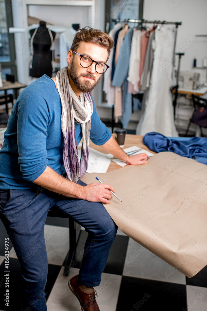 一位英俊的时装设计师坐在充满剪裁的工作室里，手里拿着纸草图的肖像