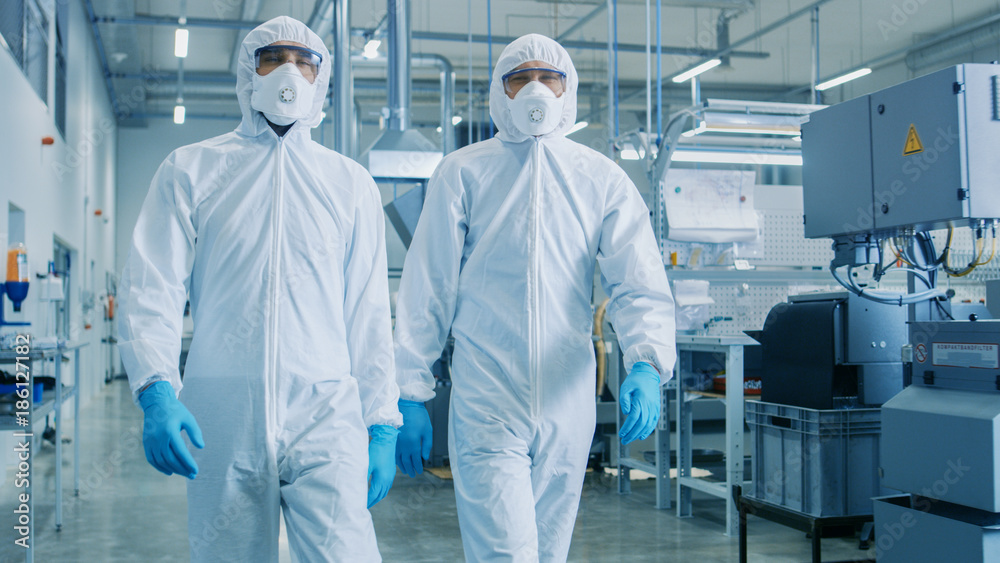 两名工程师/科学家穿着危险品无菌服走进技术先进的工厂/