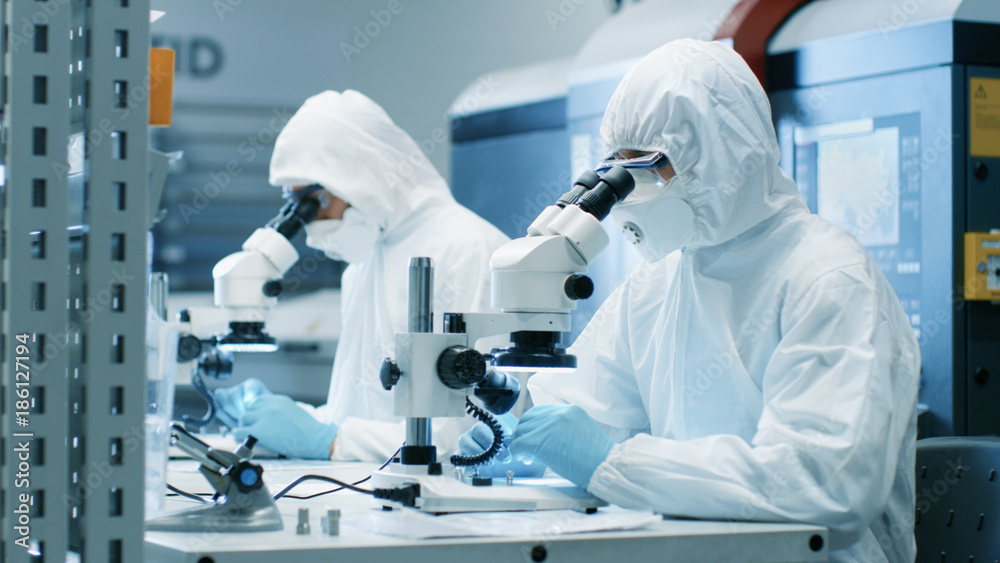 两名穿着无菌洁净室套装的工程师/科学家/技术人员使用显微镜进行组件调整