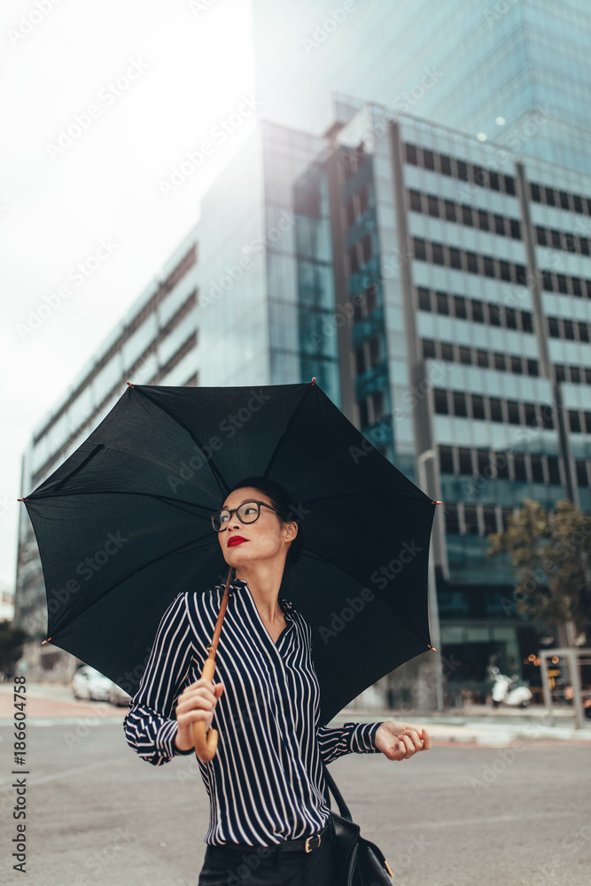 撑着雨伞走在城市街道上的亚洲女商人