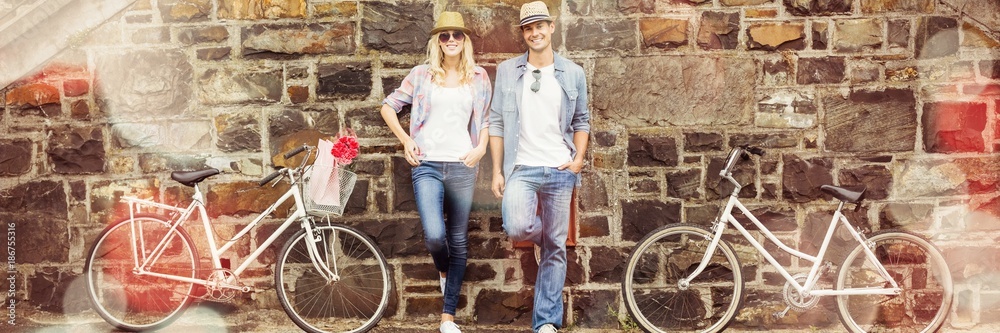 时髦的年轻夫妇骑着自行车站在砖墙旁