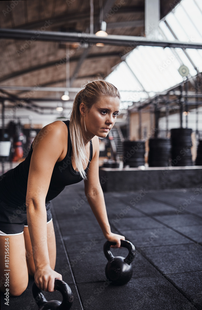 健康的年轻女性在健身房地板上进行举重锻炼