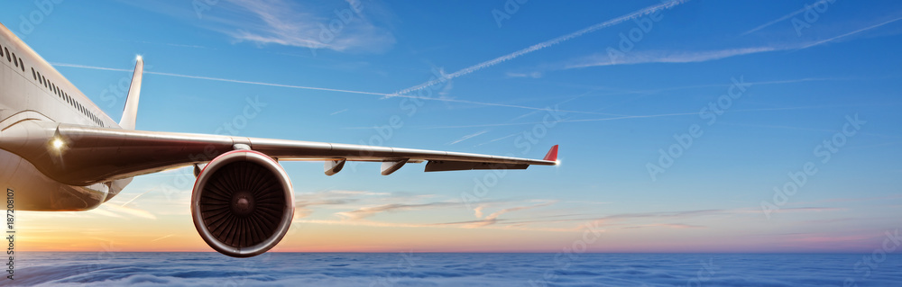 在美丽的日落光线下，商业飞机喷气式客机在云层上方飞行的机翼细节。