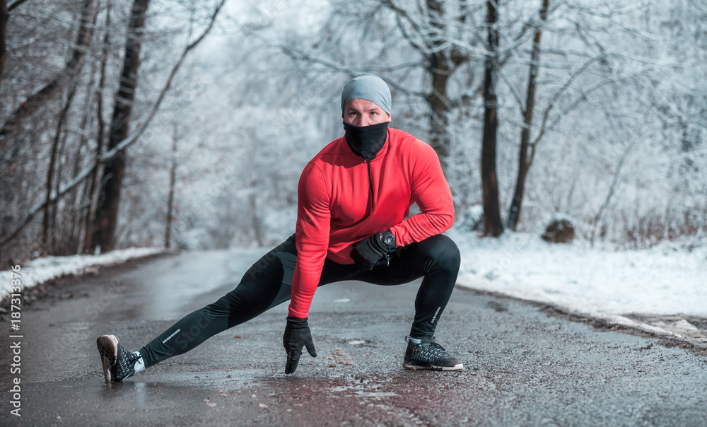 冬季跑步运动，跑步者在雪地森林的道路上伸展身体