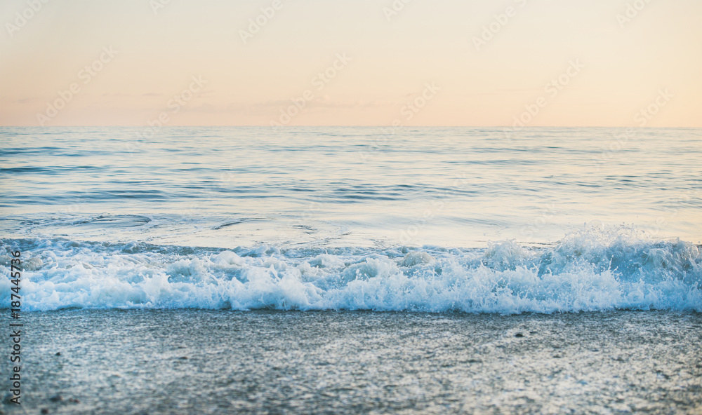 日落时平静的大海和卵石海滩的景色，柔和的颜色