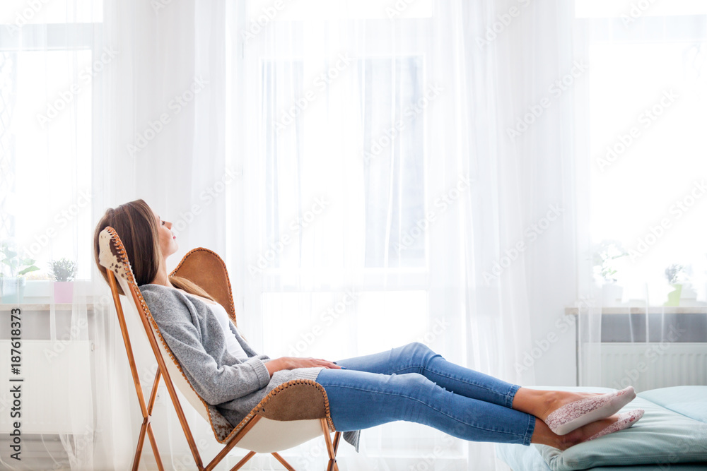 家里的女人坐在靠近窗户的现代椅子上，在客厅放松