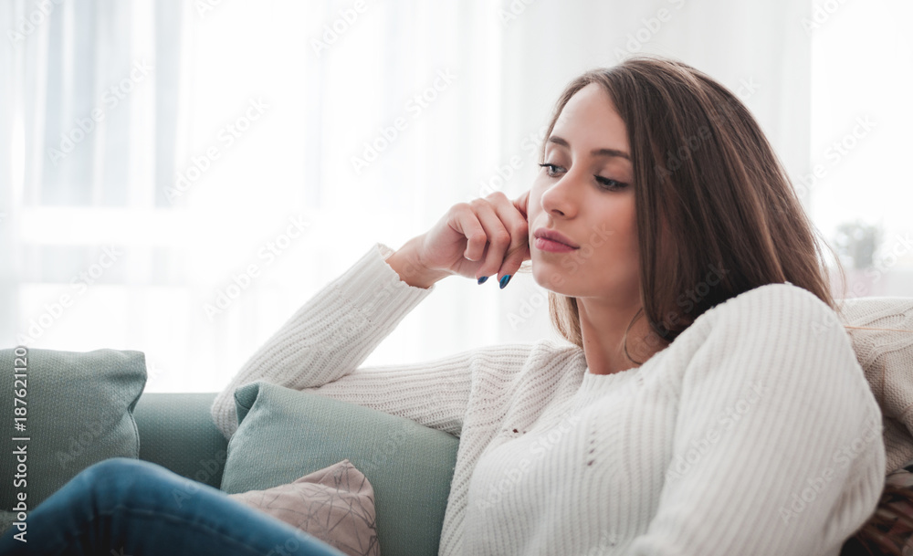 悲伤的女人坐在家里的沙发上沉思，思考概念