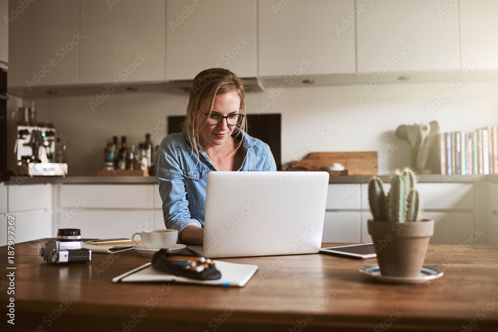 Young woman working online in her kitchen with a laptop