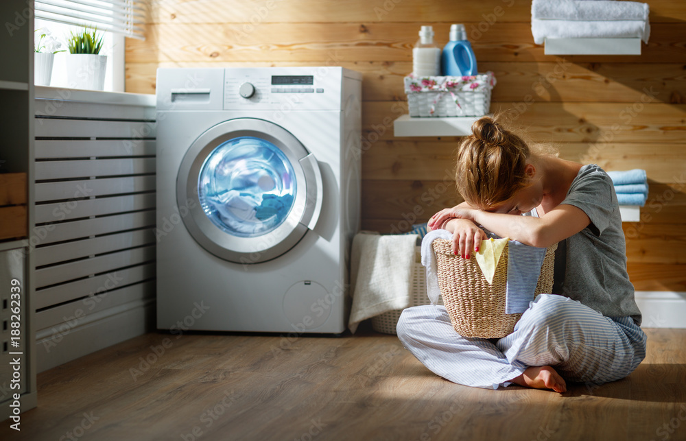 疲惫的家庭主妇在压力下睡在带洗衣机的洗衣房里。