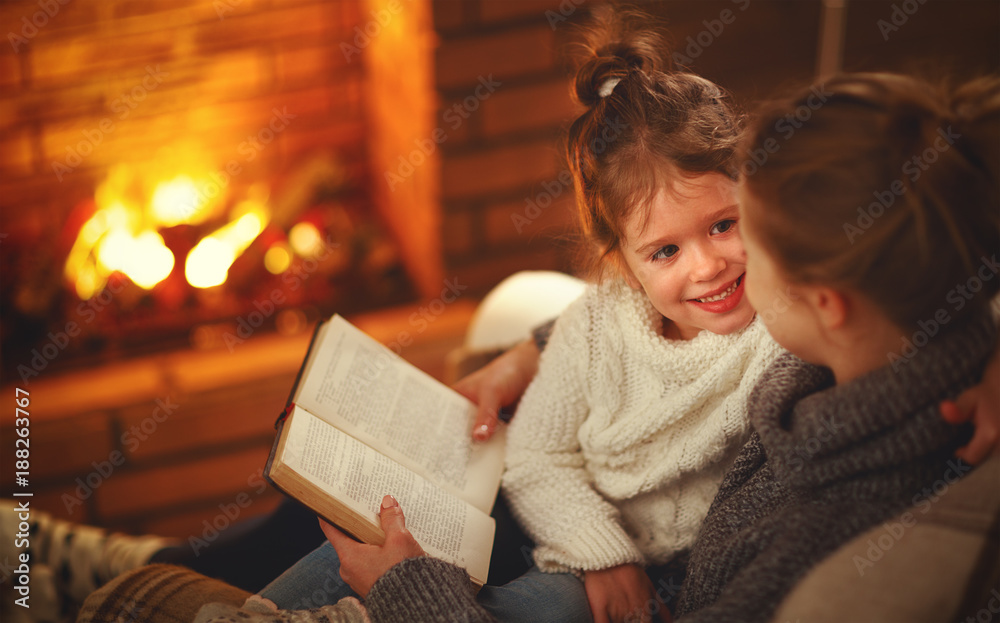 happy family mother and child daughter read book on winter evening near fireplace.