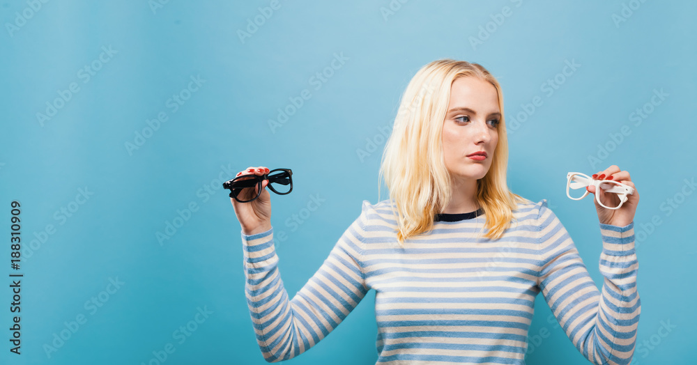 Young woman choosing between contact lenses or glasses on a solid background