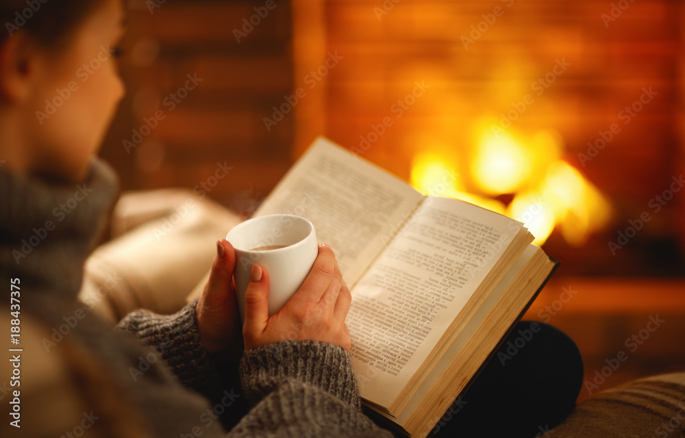 冬天晚上，女孩手里拿着一本书和一杯咖啡，靠近壁炉