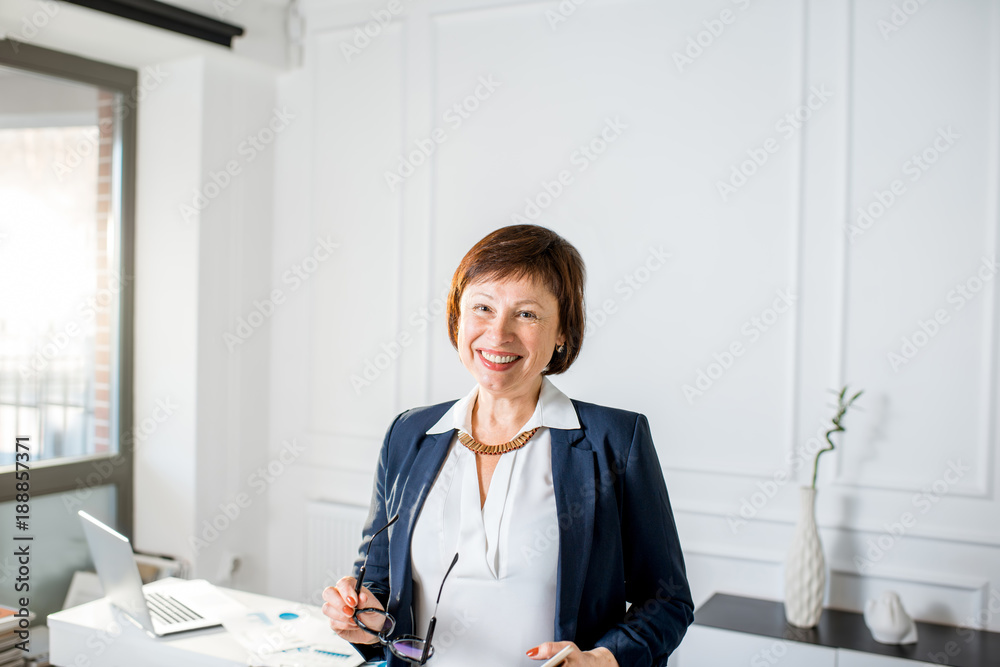 一位穿着西装的优雅高级女商人站在白色办公室的肖像