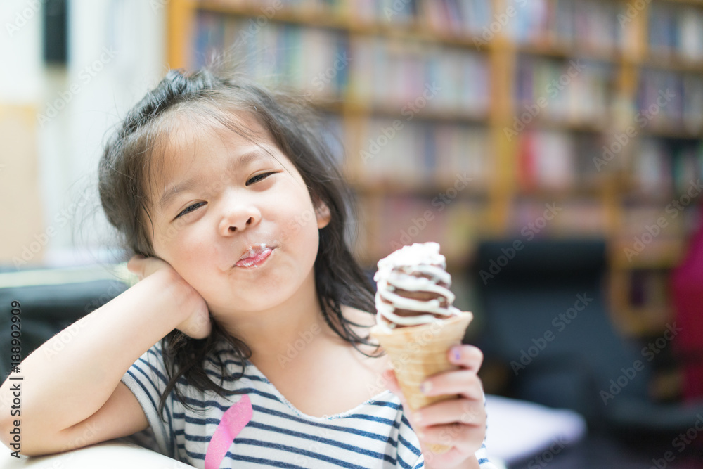 快乐的亚洲小女孩吃着软奶油或冰淇淋，坐在客厅的沙发上。
