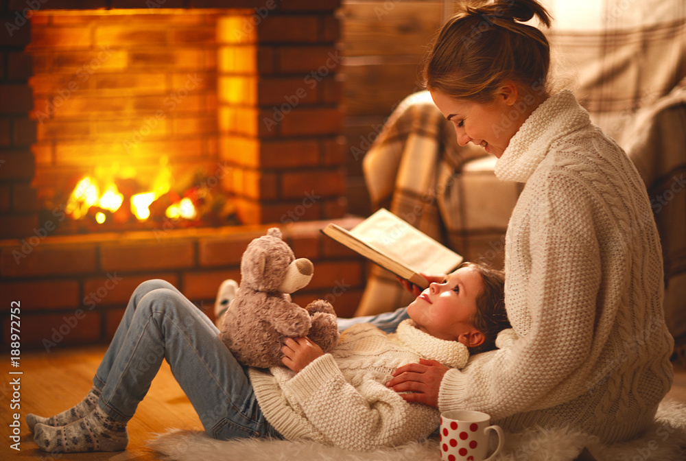 家庭母亲和孩子在冬天的晚上在壁炉旁看书。