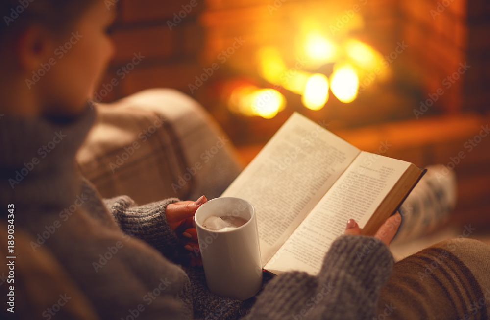 冬天晚上，女孩手里拿着一本书和一杯咖啡，靠近壁炉
