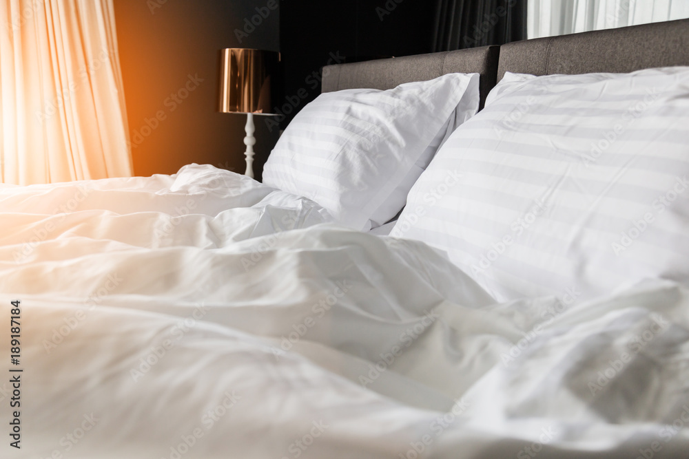卧室内部晨光中未经整理的褶皱床，配有白色凌乱的枕头