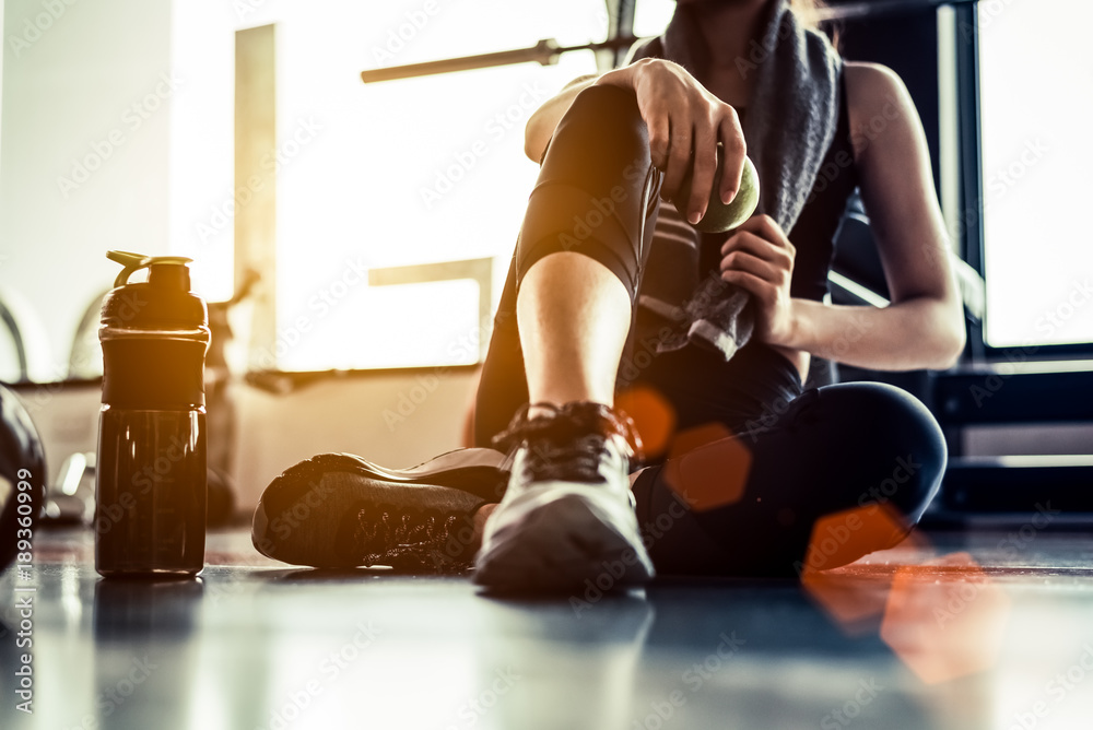 运动女性在锻炼后坐着休息，或在健身馆用蛋白奶昔或饮料锻炼