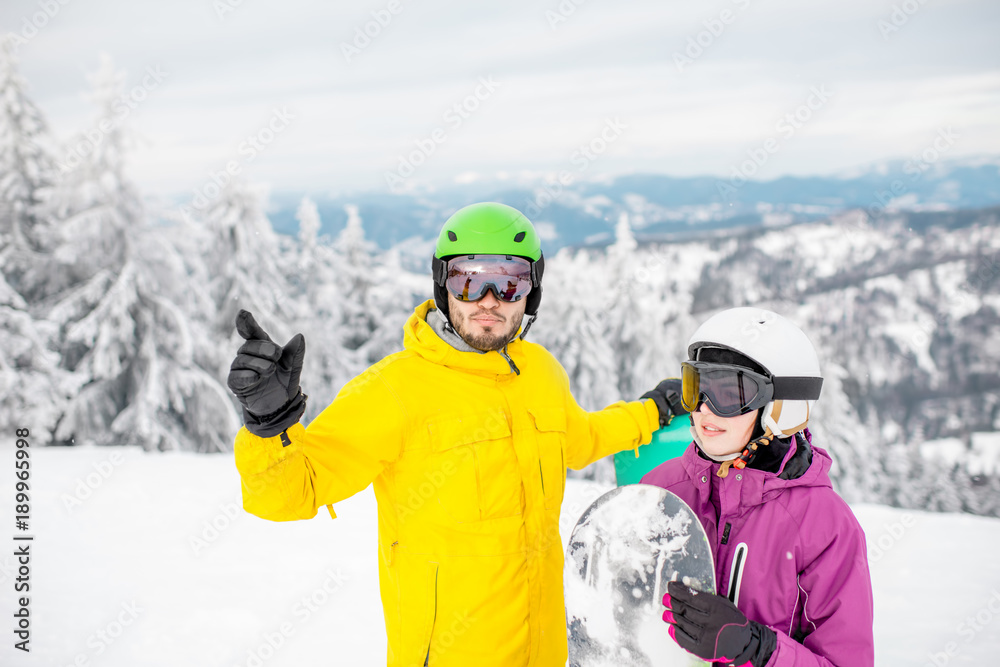 一对穿着冬季运动服的年轻夫妇在冬季与滑雪板站在一起交谈