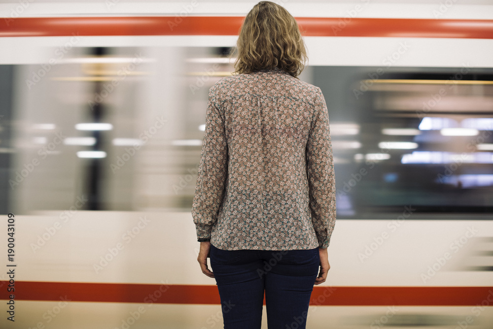 一名金发女子在火车站台等候的后视图
