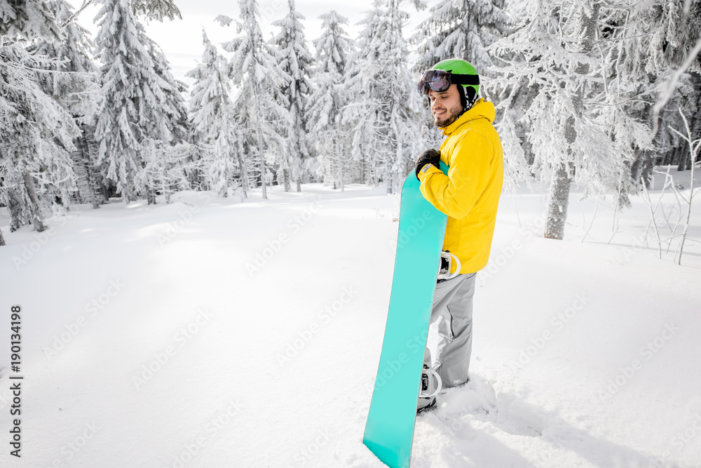 一个穿着冬装的男人拿着滑雪板站在美丽的白雪覆盖的冷杉林中的肖像