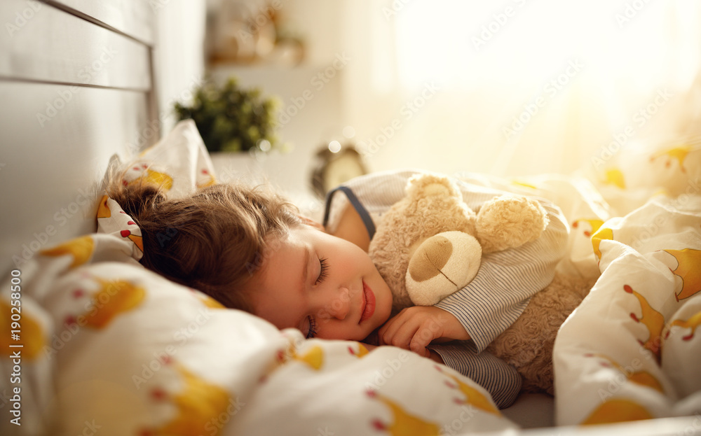 小女孩早上抱着玩具泰迪熊睡在床上