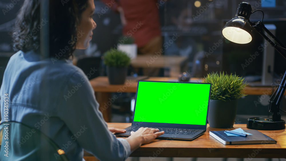 女上班族在办公桌上用一台带绿色屏幕的笔记本电脑工作。肩扛着脚
