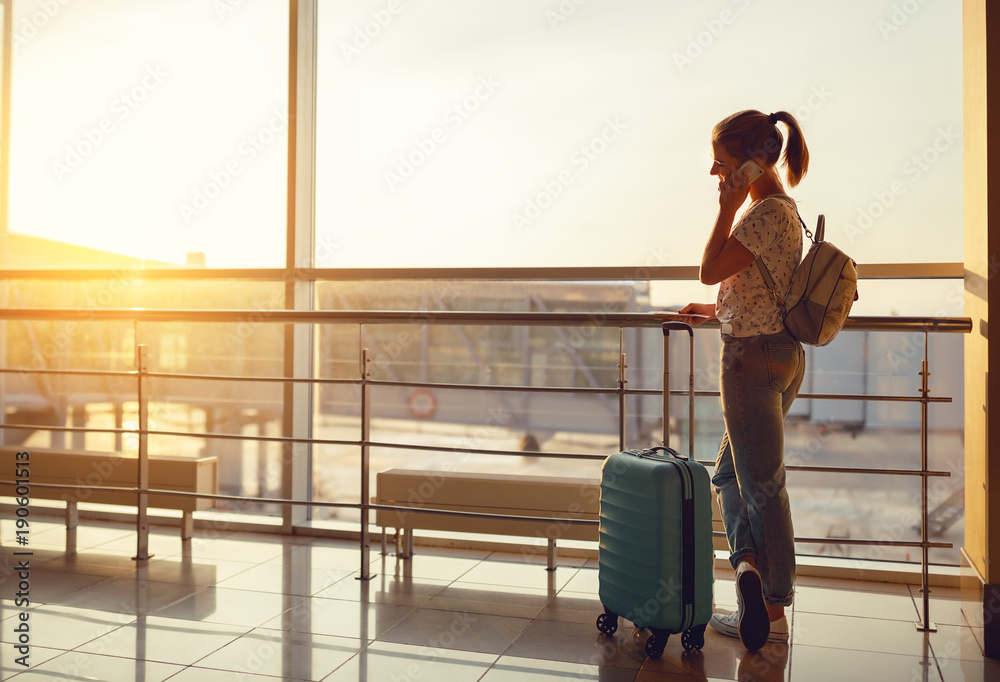 一名女子提着行李箱在机场窗口打电话等待飞行