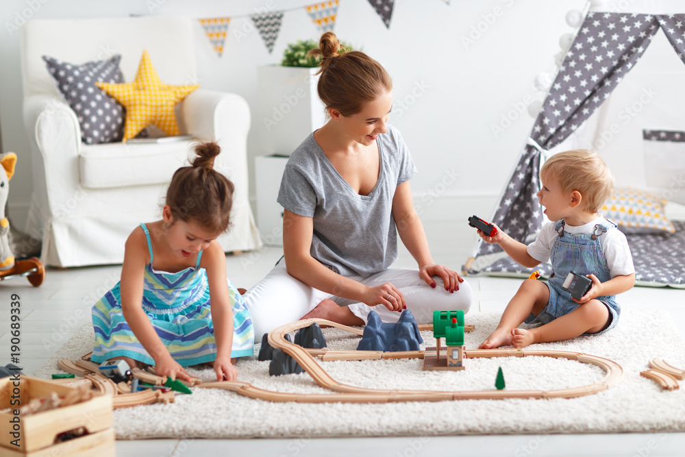 家庭母亲和孩子在游戏室玩玩具铁路。