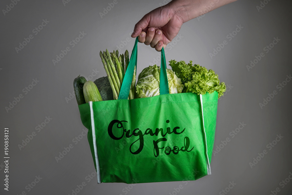 close up a hand holding green grocery bag with Organic Food text of mixed  organic green vegetables 