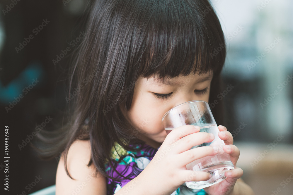 快乐可爱的小女孩在喝水。微笑的亚洲孩子手里拿着透明玻璃。