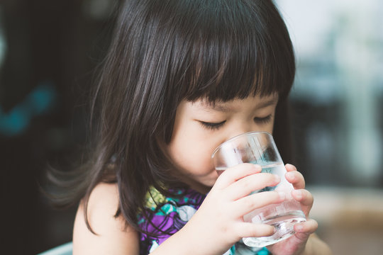 快乐可爱的小女孩在喝水。微笑的亚洲孩子手里拿着透明玻璃。